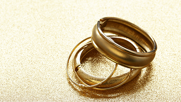 Image: Four gold rings lying in a stack on gold textured paper. 