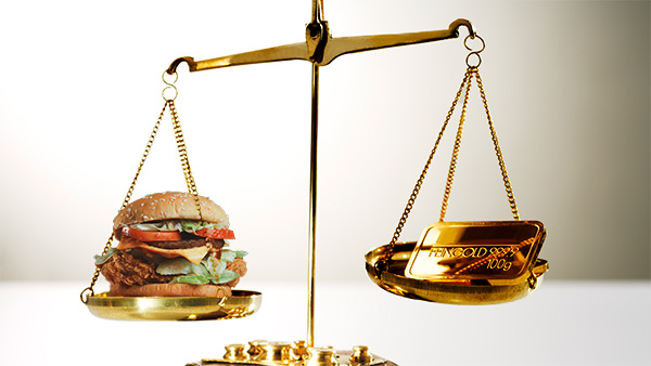 Image: A burger measured against a bar of gold on a weighing scale.