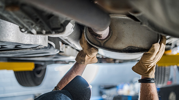 Image: A mechanic replacing the catalytic converter on a car.
